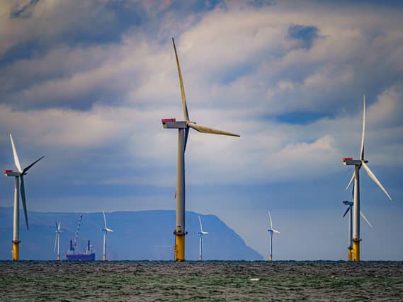 Offshore wind turbines stand in the sea with the coast in the background under a cloudy sky