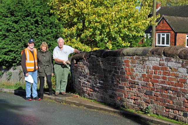 Bob Wood, Rosalind Wells and Bob's father, Joseph Eric Wood, next to a wall on Burton Road, which has been damaged due to lorries trying to reverse along the narrow road