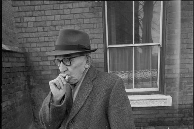 An elderly man takes a drag on a cigarette