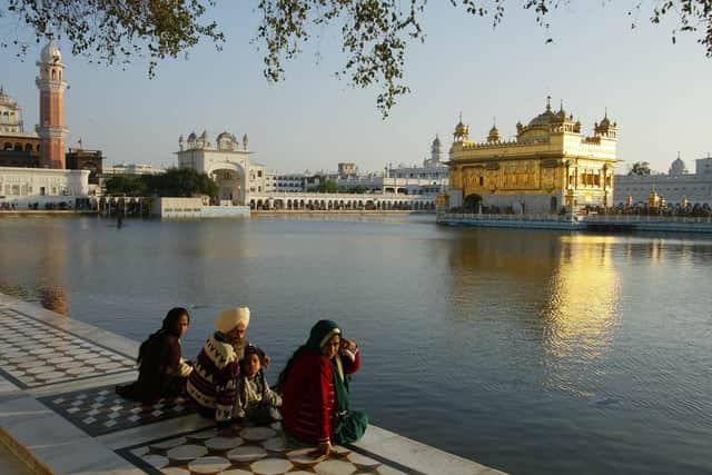 Pilgrims sit at the edge of the moat surrounding the Golden Temple of Amritsar