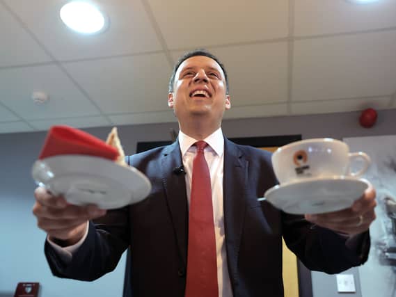 Anas Sarwar smiling while holding a cup in one hand, and a plate in the other