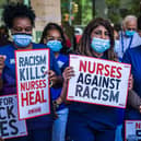 A group of nurses in blue scrubs holding placards which read 'Nurses against racism' and 'Racism kills, nurses heal'