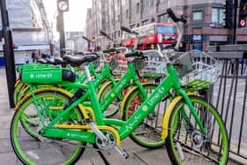 A number of green Lime bikes lined up on a pavement, with a red London bus in the background