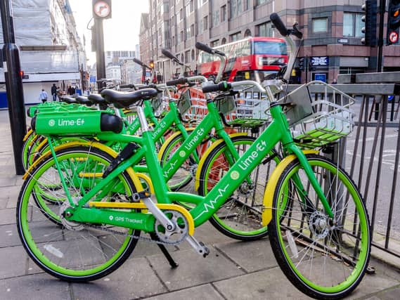 A number of green Lime bikes lined up on a pavement, with a red London bus in the background