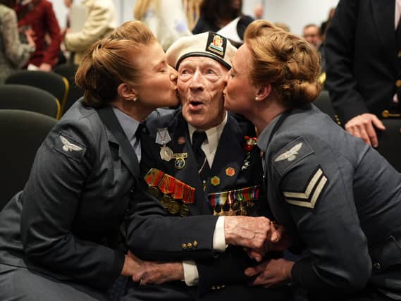 Alec Penstone in Navy uniform being kissed on both cheeks by two women in uniform