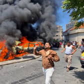 People run in front of burned cars that were attacked in an Israeli airstrike in the southern port city of Sidon, Lebanon