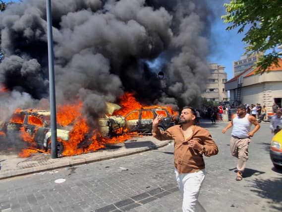 People run in front of burned cars that were attacked in an Israeli airstrike in the southern port city of Sidon, Lebanon