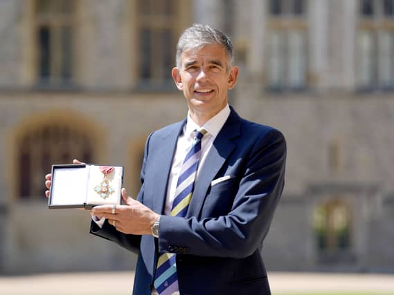 Matthew Brittin smiling while holding up his CBE medal