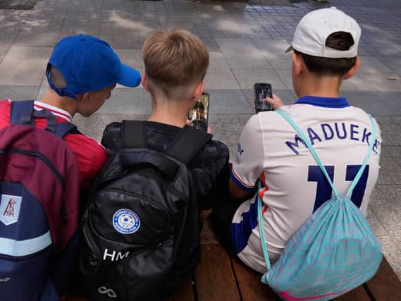 Three boys using their phones while sitting outside a school in Sydney