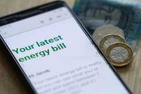 An online energy bill displayed on a smartphone sitting on a table next to some coins and a five pound note