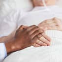 Visitor's hand holding a patient's hand on a hospital bed