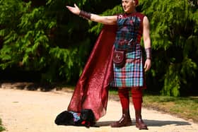 Alan Cumming wearing a tartan outfit, with one arm outstretched