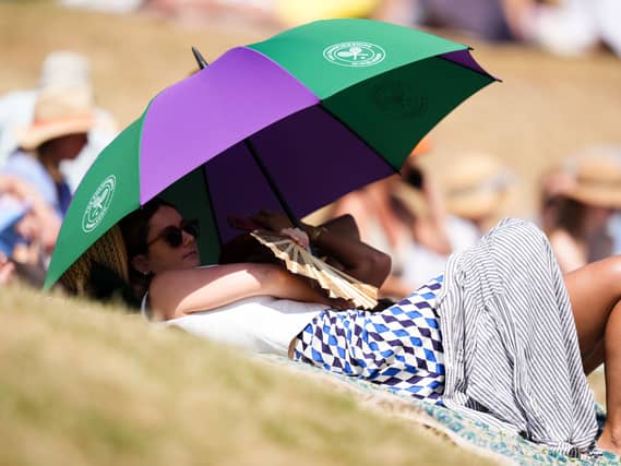 A woman uses a Wimbledon umbrella to shade herself while lying on grass