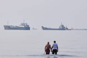 Two men wade in the waters of the Strait of Hormuz with vessels anchored in the background (Razieh Poudat/AP)