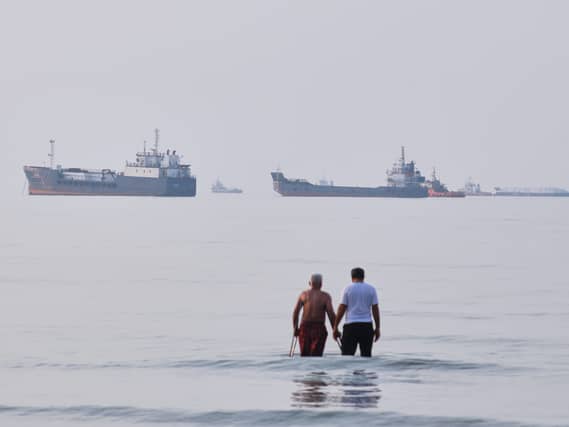 Two men wade in the waters of the Strait of Hormuz with vessels anchored in the background (Razieh Poudat/AP)