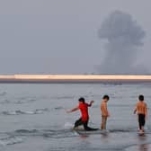 Three boys play in the shallow waters of the Strait of Hormuz, as a plume of smoke rises from an explosion in the background