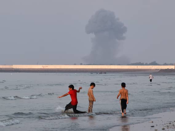 Three boys play in the shallow waters of the Strait of Hormuz, as a plume of smoke rises from an explosion in the background