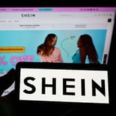 A phone with the Shein logo held in front of the website's homepage