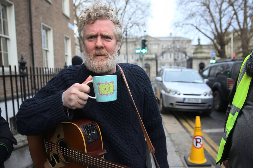 Glen Hansard holding a coffee mug with a guitar slung over his shoulder