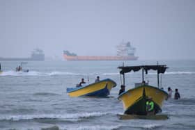 Small boats line the shore as cargo ships and other commercial vessels appear anchored in the Strait of Hormuz