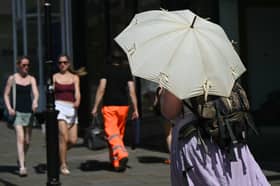 A person shelters from the heat of the sun beneath a parasol umbrella, in Guildford, on 25 June 2026.