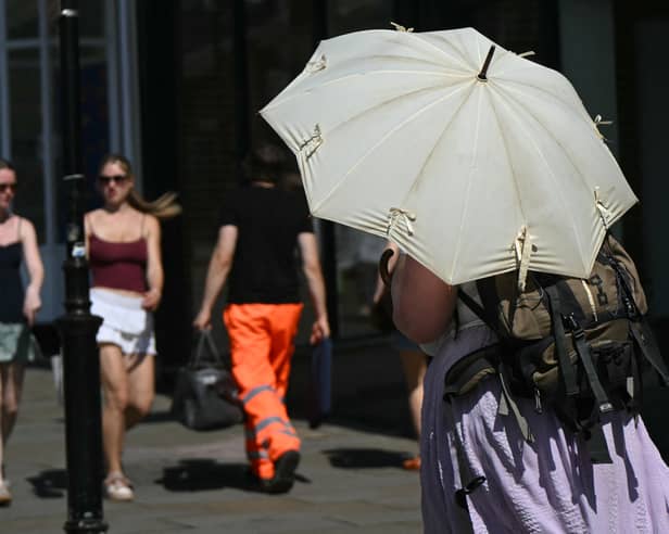 A person shelters from the heat of the sun beneath a parasol umbrella, in Guildford, on 25 June 2026.
