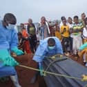 People dressed in protective gear lower a coffin into a grave