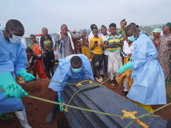 People dressed in protective gear lower a coffin into a grave