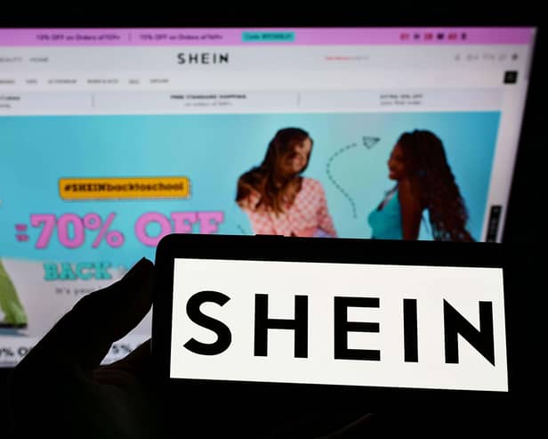 A phone with the Shein logo held in front of the website's homepage