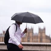 A man using an umbrella while walking, with the Houses of Parliament in the background