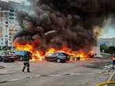 Firefighters tackle cars on fire, with thick black smoke rising above them