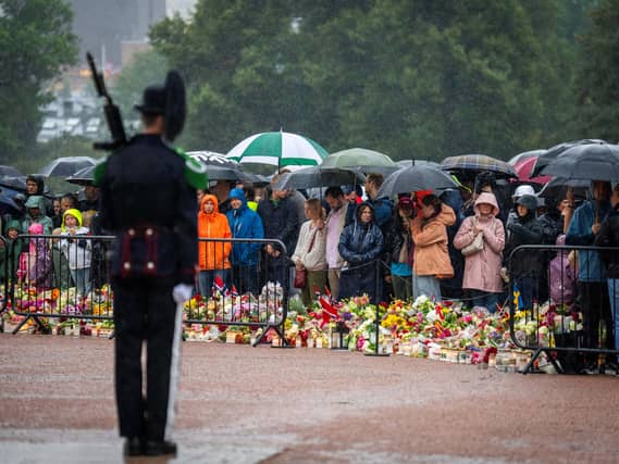 Mourners under umbrellas, with floral tributes on the ground in front of them