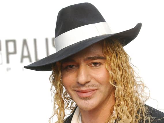 John Galliano wearing a black and white hat and black jacket with white scarf.