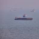 A small boat sails past cargo ships and other commercial vessels anchored in the Strait of Hormuz