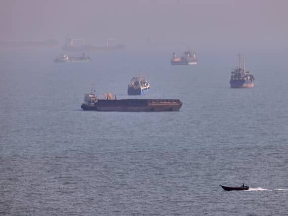A small boat sails past cargo ships and other commercial vessels anchored in the Strait of Hormuz