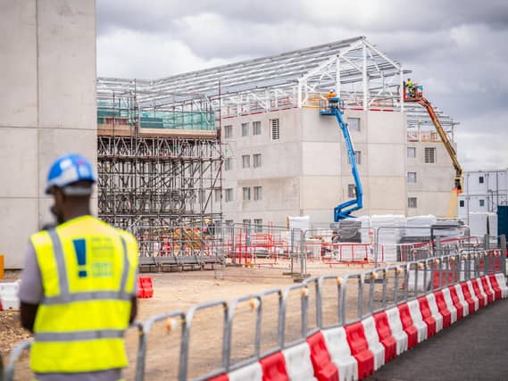 A person in a high-vis jacket and helmet with a prison construction site in the background