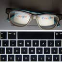 A pair of glasses on a laptop keyboard reflecting the Google logo
