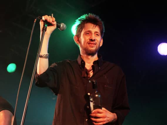 Shane MacGowan smiling while on stage, holding a microphone stand