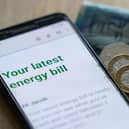 An energy bill displayed on a smartphone, next to coins and notes
