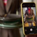 A mobile phone in the foreground taking a picture of some crockery being held by a woman
