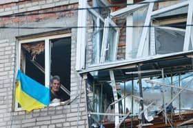 A man looks through a broken window in a residential house bearing a Ukraine flag