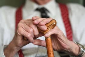 The hands of an elderly man resting on a walking stick