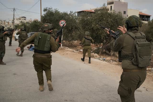 Israeli soldiers move toward a Palestinian man lying wounded on a road after they shot him following a settler attack on Palestinians harvesting olives in Abu Falah (Leo Correa/AP)