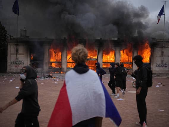 A protester wraps a French flag around them in front of the burning tourism office during a demonstration against rising living costs and in solidarity with students’ grievances in Lyon, France