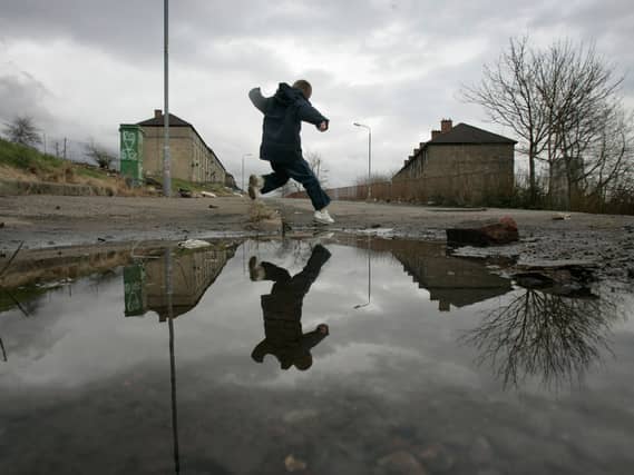 A boy jumping over a large puddle in waste land, with housing in the background