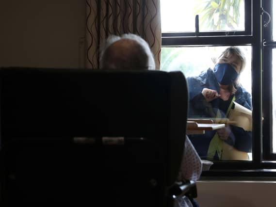 An elderly resident talks to a visitor through the window at nursing home