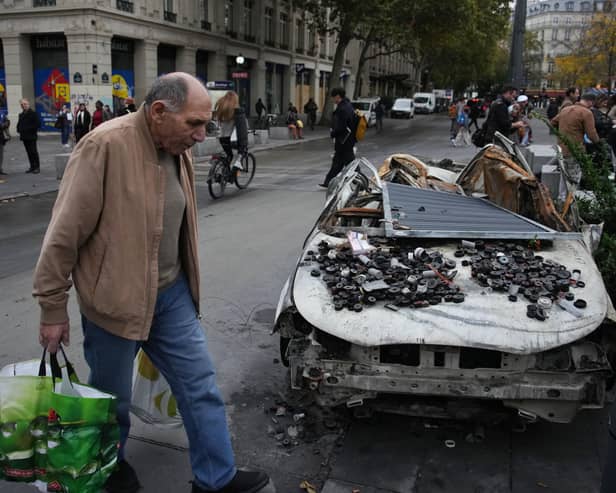 A man walks past a burned-out car in Paris after a quiet Monday night under curfew