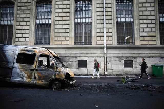 Passers-by walk past burned-out cars in Paris (Christophe Ena/AP/PA)
