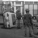 Troops on patrol in the Falls Road area of Belfast encounter a civilian by an overturned car that formed a barricade during rioting in 1981