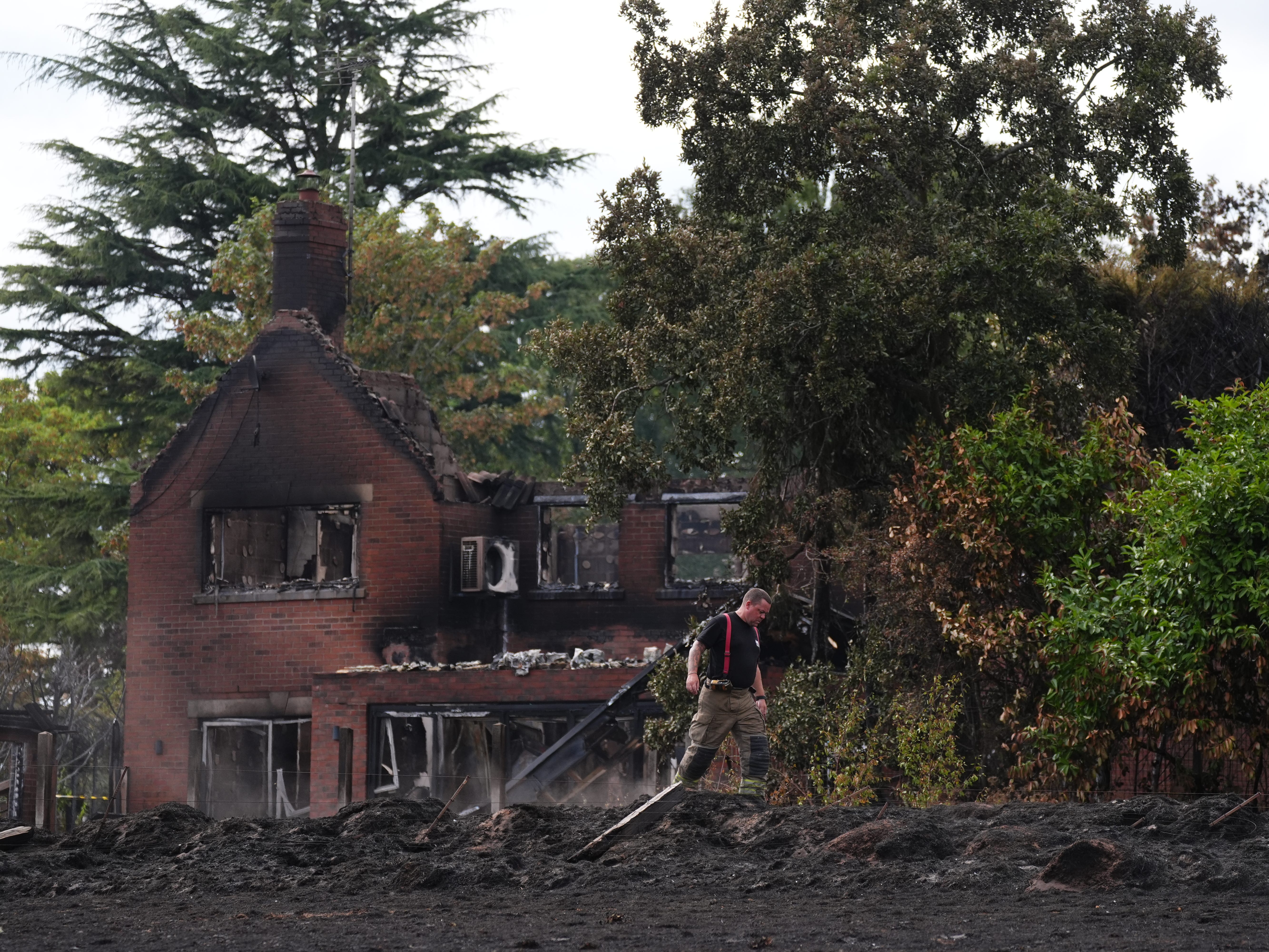 A firefighter outside the burnt-out remains of a house